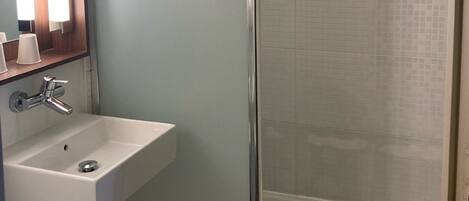 A bathroom with a glass shower enclosure, a sink with a mirror, and a towel rack.