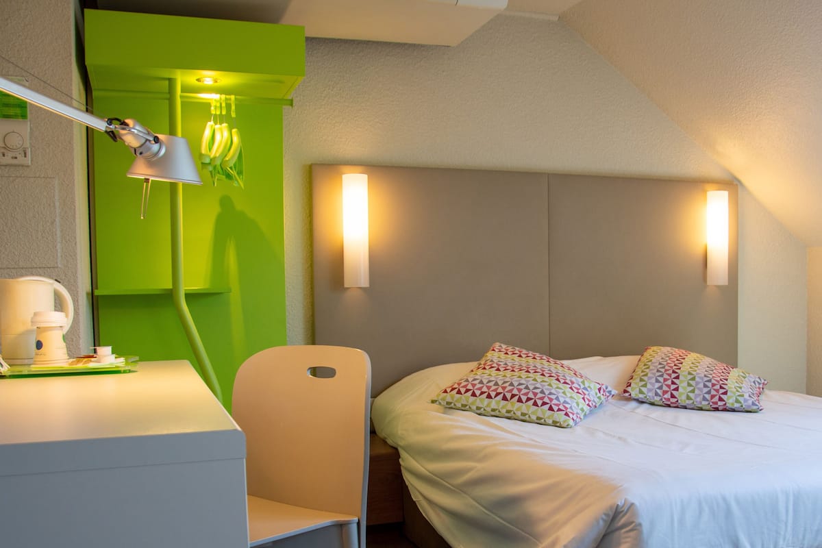 Une chambre d’hôtel avec un lit, un bureau, une chaise, une lampe et un mur d’accent vert.