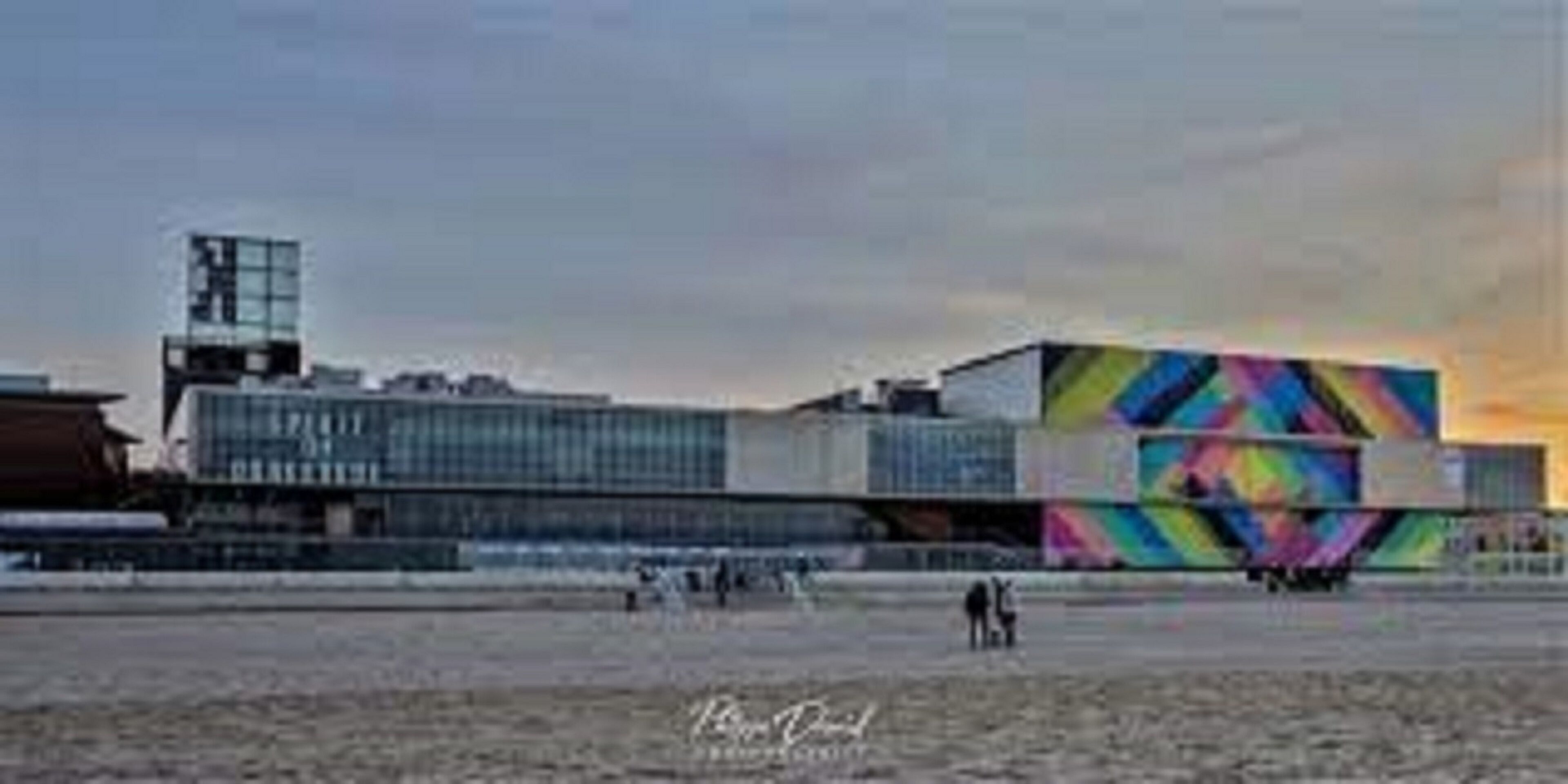 Un edificio moderno con fachada geométrica y un mural grande y colorido.