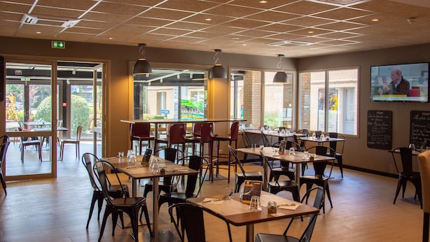 Un restaurante con varias mesas y sillas, un techo con diseño de rejilla y amplias ventanas que dejan entrar luz natural.