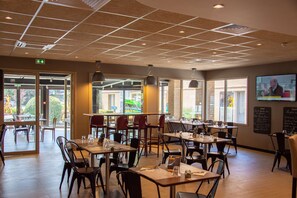 Un restaurante con varias mesas y sillas, un techo con diseño de rejilla y amplias ventanas que dejan entrar luz natural.