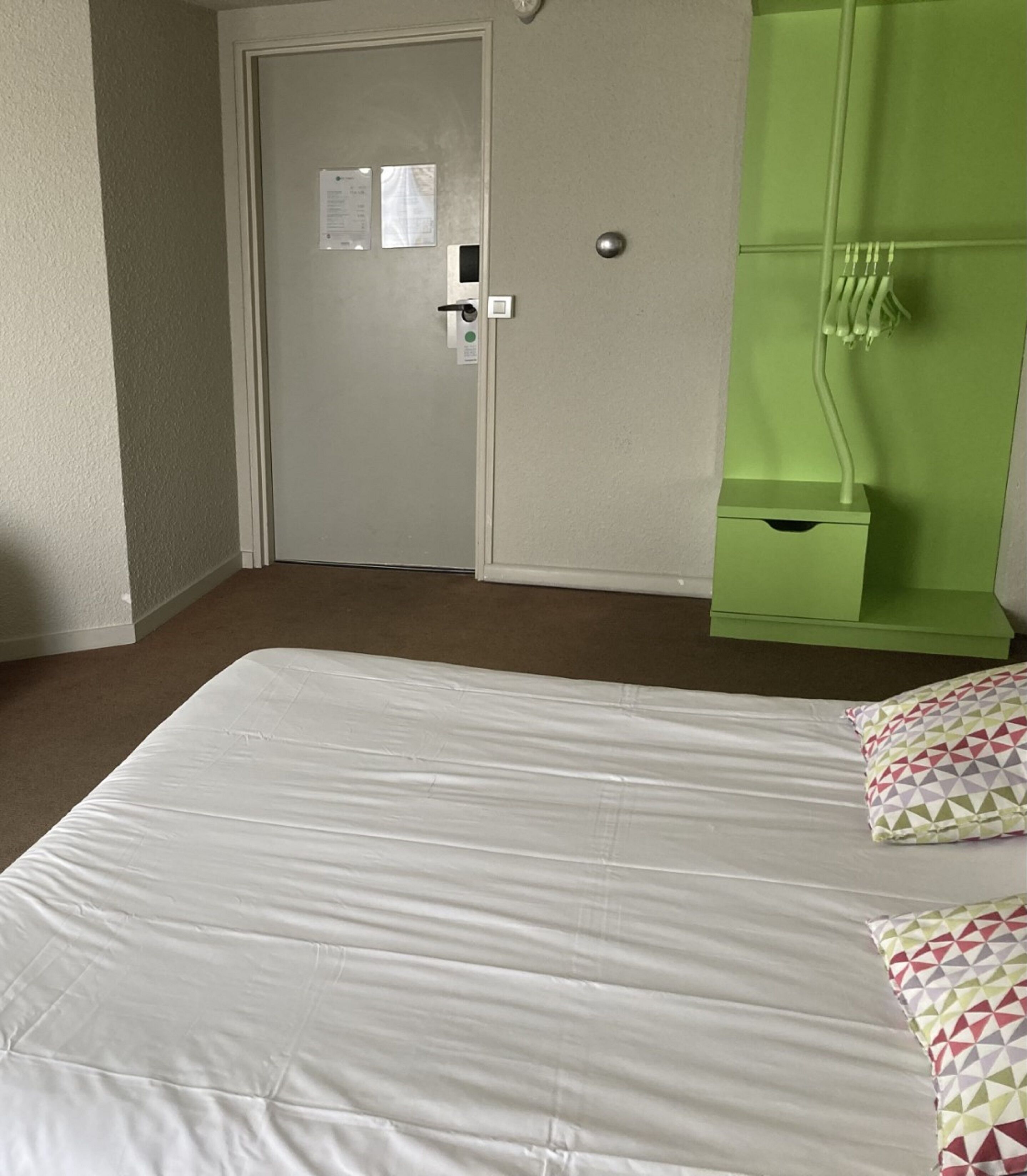 Habitación de hotel con cama, baño verde y puerta con cerradura y un cartel pequeño.