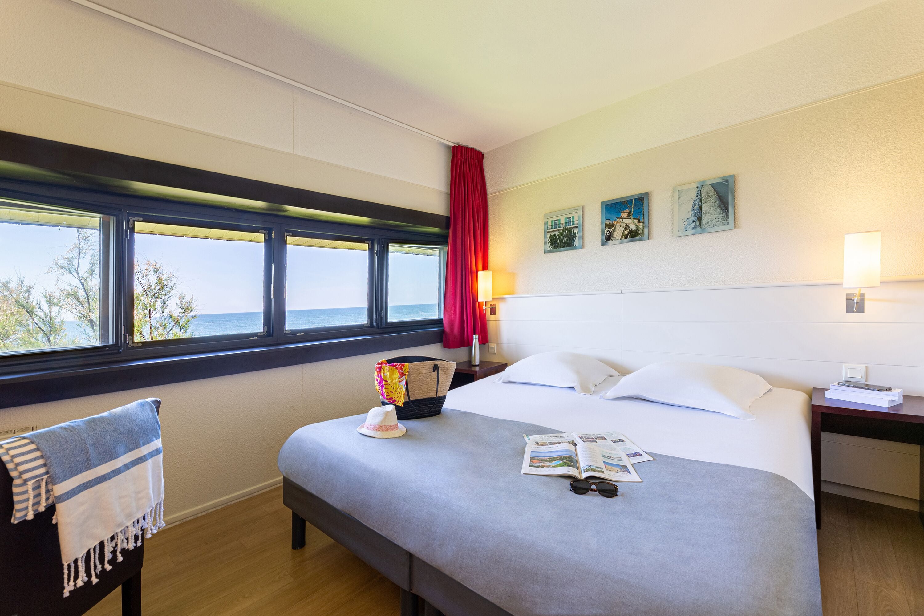 Habitación de hotel con cama, mesita de noche, lámpara, ventana con vistas y silla con una toalla.