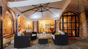A cozy outdoor seating area with wicker furniture, a large umbrella, and stone flooring. - Country Hotel Borgo Sant'Ippolito (Lastra a Signa)