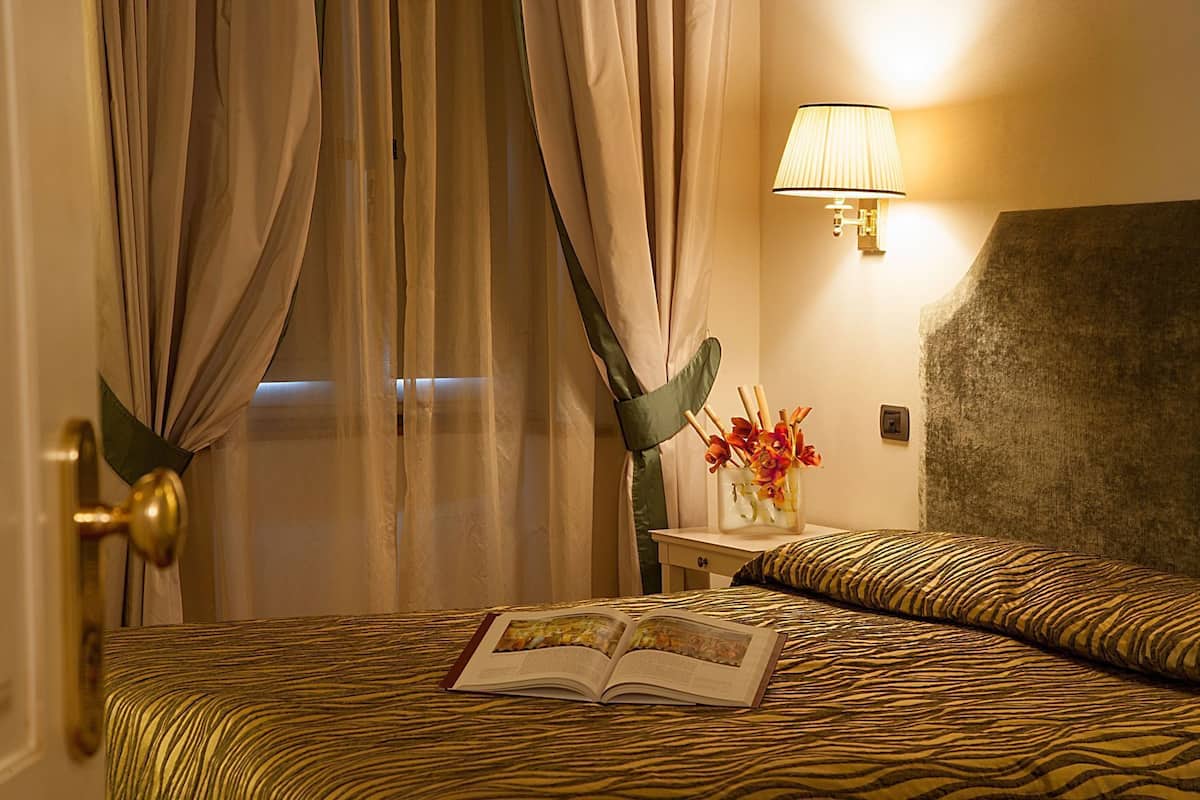 Una habitación de hotel con una cama, una mesita de noche con lámpara y una ventana con cortinas.