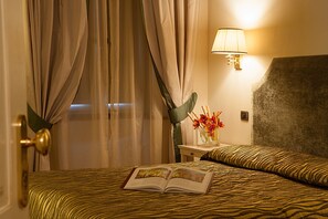 Une chambre d’hôtel avec un lit, des rideaux, une lampe et un vase de fleurs.