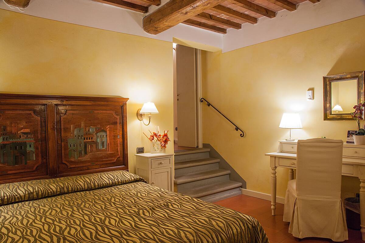 Un dormitorio con cama, mesita de noche, escritorio, silla, escalera y espejo.