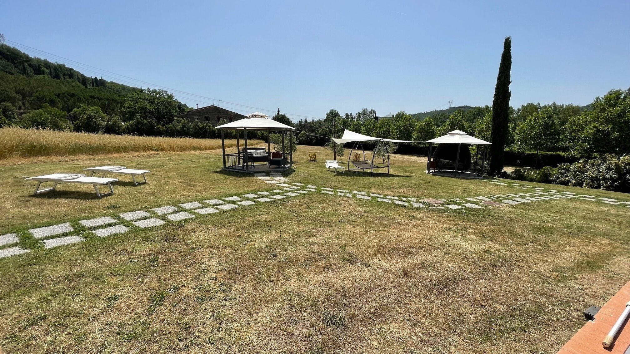 Un espacio al aire libre con tres gazebos, un camino de piedra y un campo cubierto de césped.