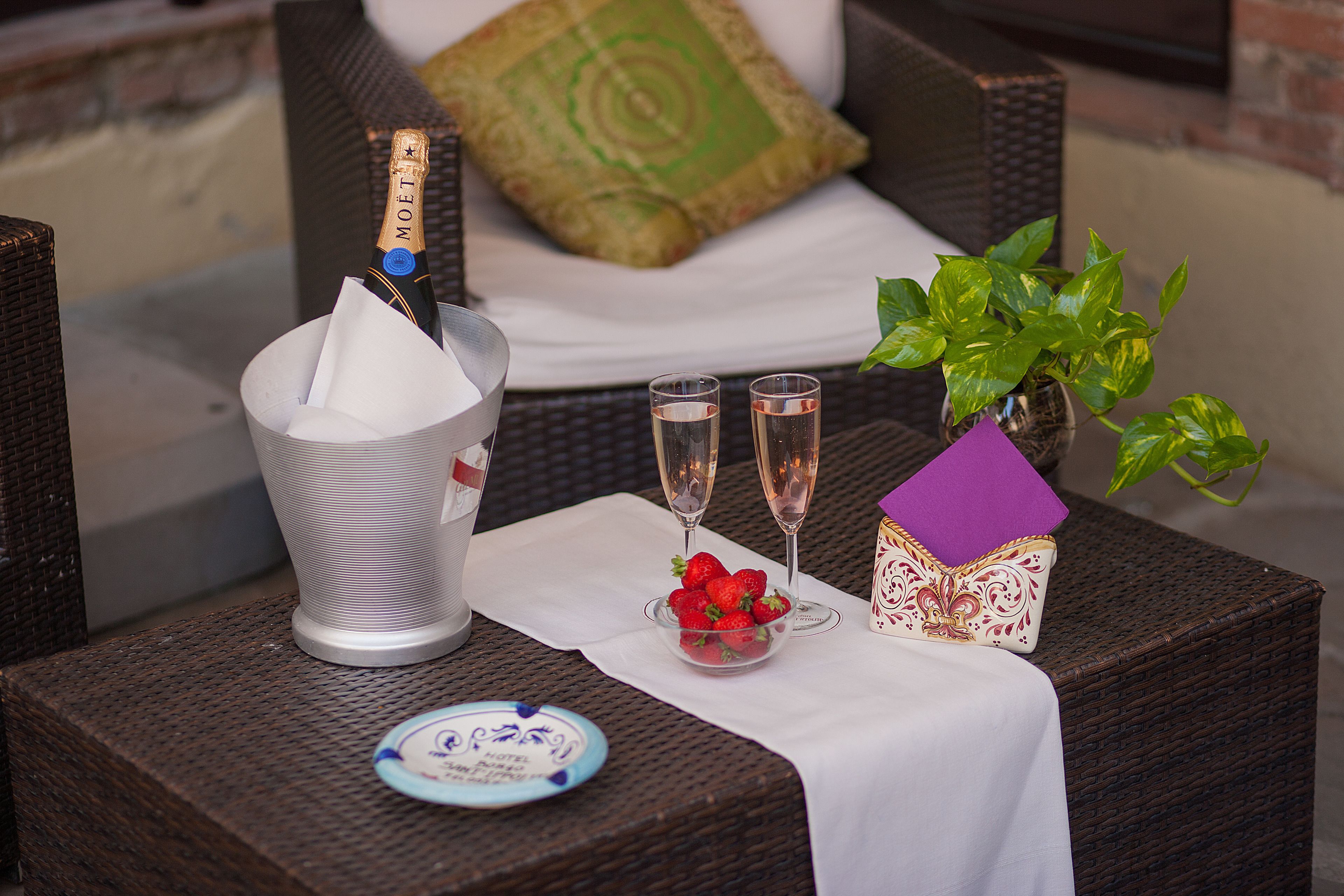 A wicker table with a bottle of champagne, two glasses, a bowl of strawberries, a decorative box, and a plate with a blue design.
