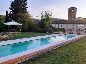 Une piscine avec une terrasse carrelée, un kiosque et du mobilier d’extérieur.
