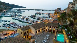 Uma marina com vários barcos atracados, um hotel com área de estar ao ar livre e piscina, e uma colina ao fundo.