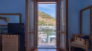 An open door leading to a balcony with a view of a marina and hills.