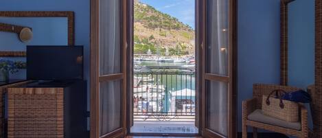 Puerta abierta que da a un balcón con vistas a un puerto deportivo y colinas.