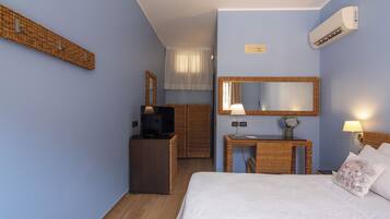 Habitación de hotel con cama, televisión, escritorio con lámpara, espejo y unidad de aire acondicionado.