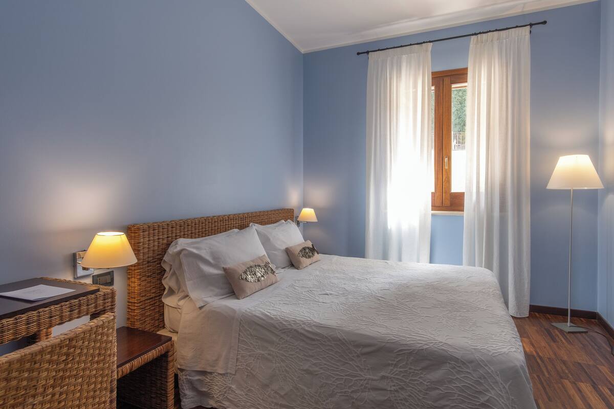 Een slaapkamer met een bed, twee nachtkastjes, een lamp en een raam met gordijnen.