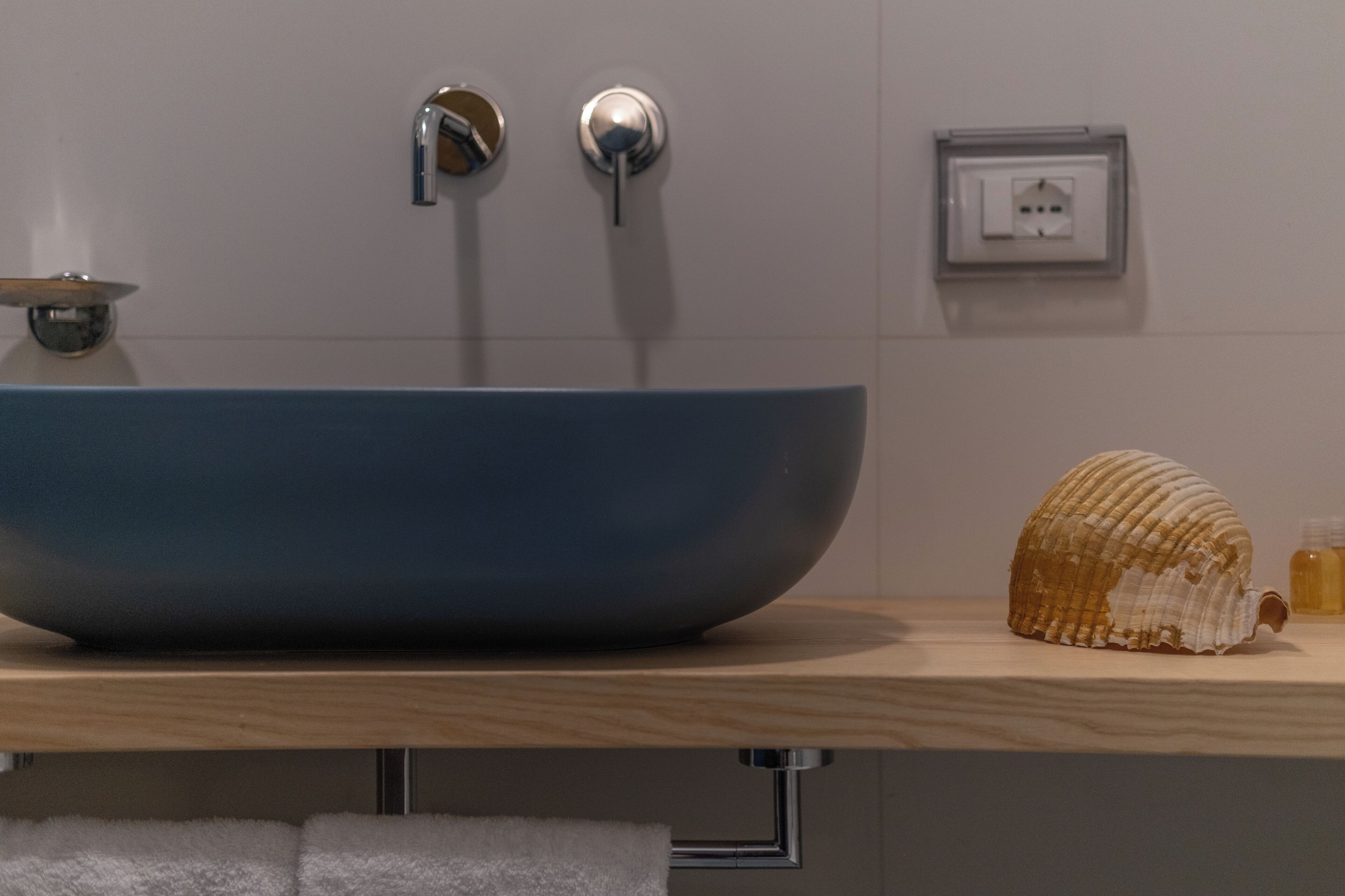 Une salle de bain avec un lavabo sur pied bleu, une serviette blanche et un coquillage posé sur le comptoir.