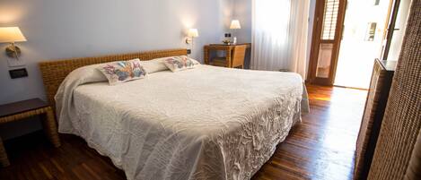 A bedroom with a large bed, bedside tables, a small desk, and a window with curtains.