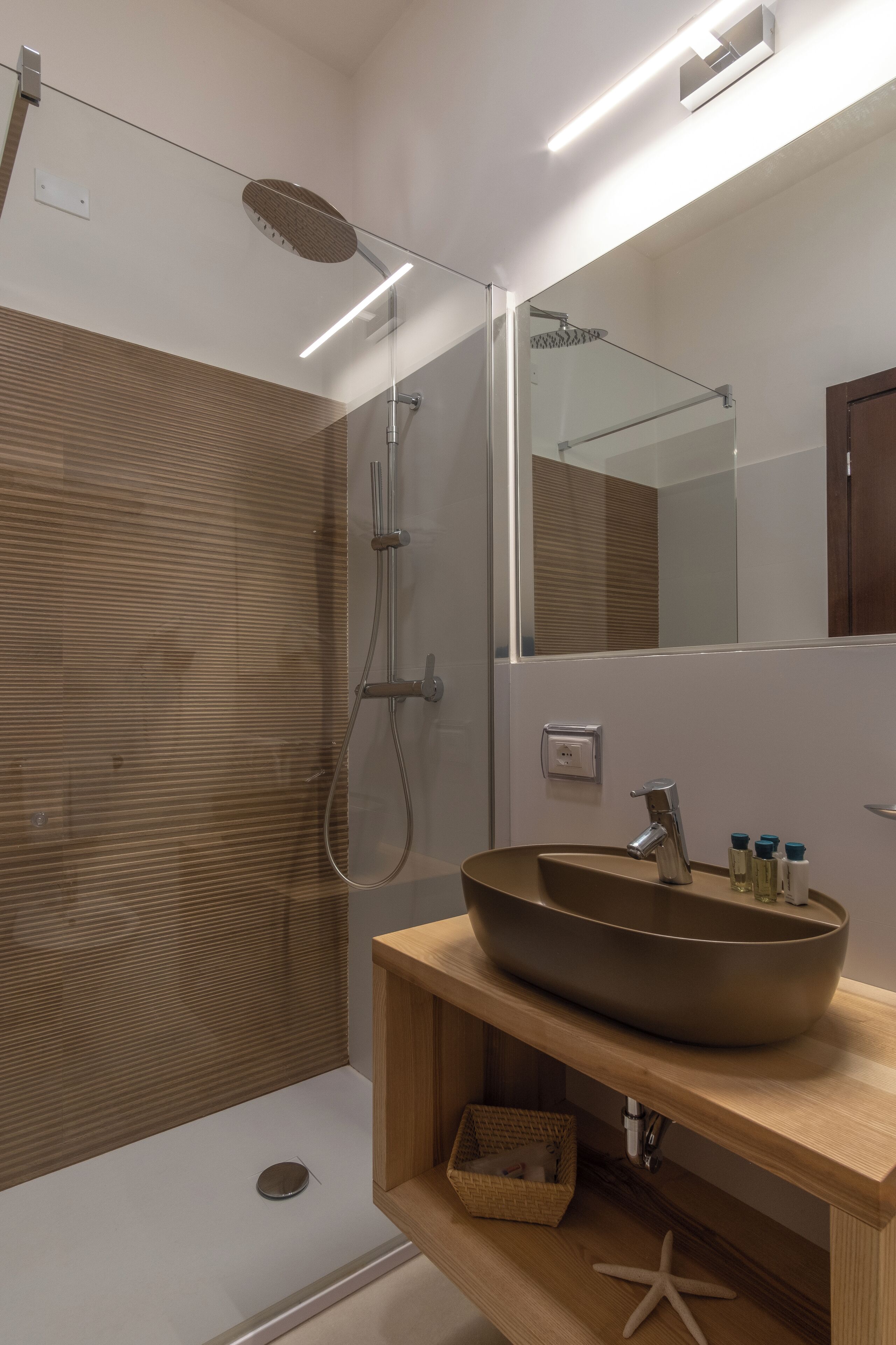 A modern bathroom with a glass-enclosed shower, a wooden vanity with a large vessel sink, and a mirror above the sink.