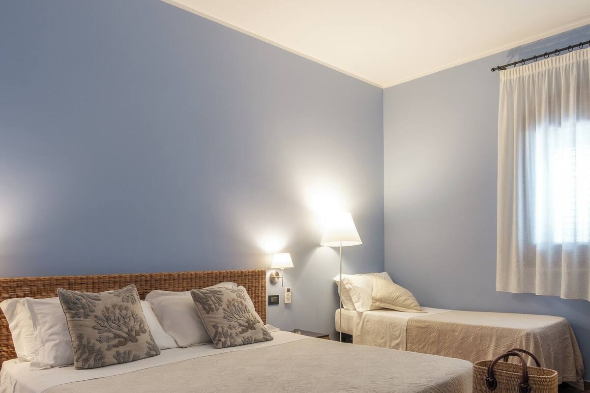 Een hotelkamer met twee bedden, een nachtkastje, een lamp en een rieten bankje.