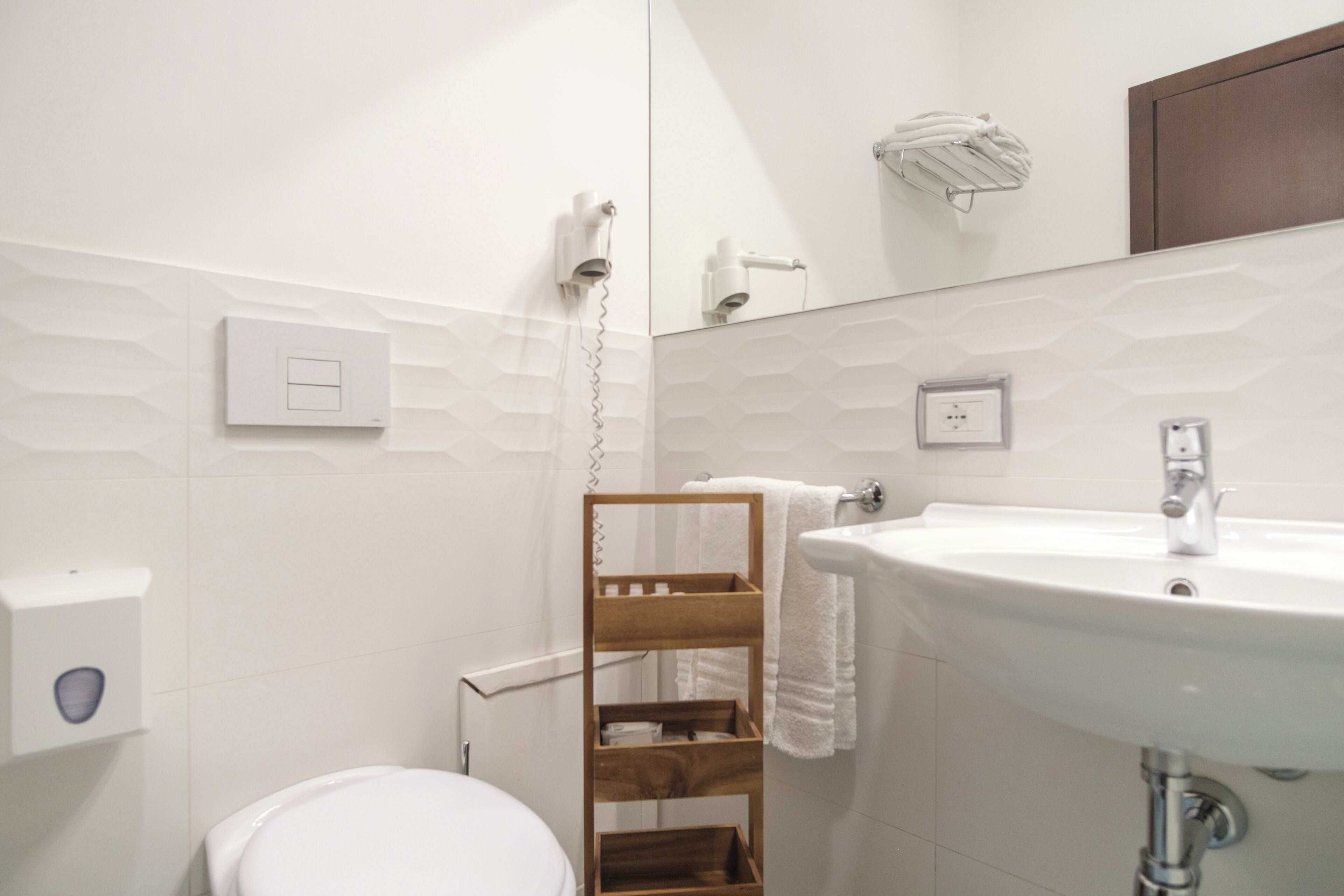 A modern bathroom with a white sink, a wooden towel rack, and a toilet.