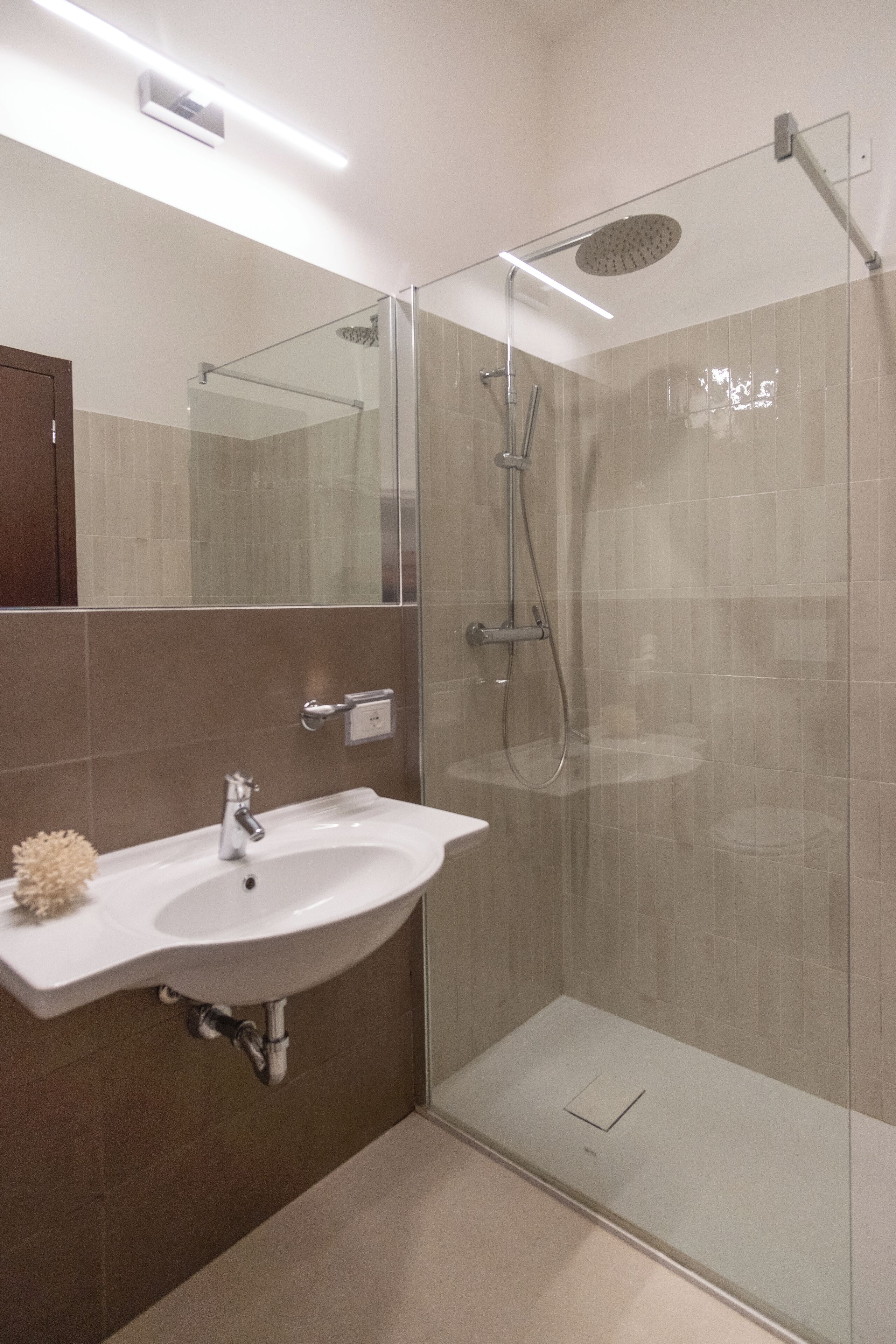 A modern bathroom with a glass-enclosed shower, a white sink, and a mirror above the sink.