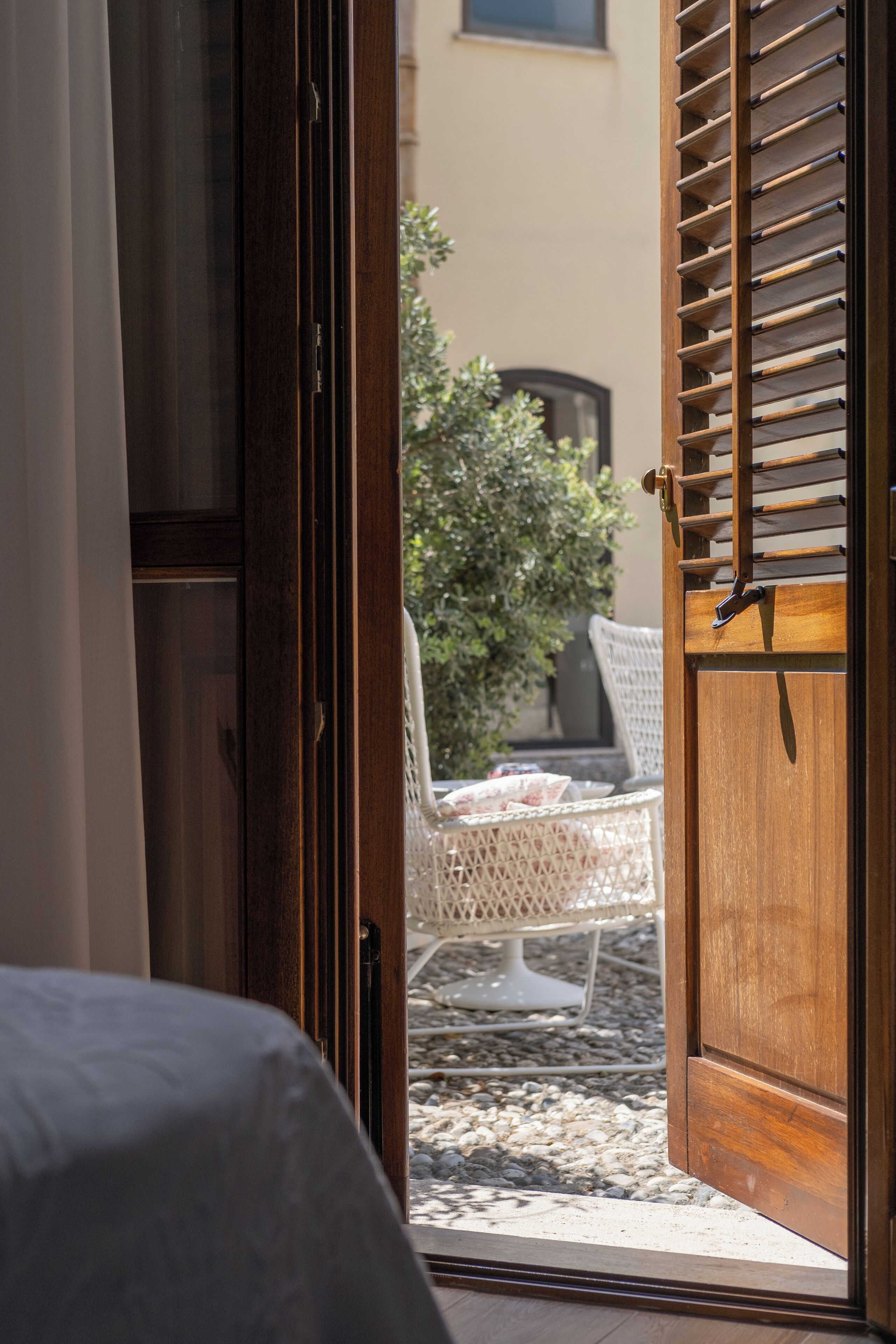 A wooden door with a latch, leading to an outdoor seating area with a white chair and table.