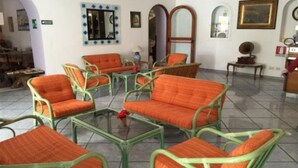 A room with green wicker furniture and orange cushions, a mirror, framed artwork, and a small table with a red object on it. - Villa Al Parco (FORIO)