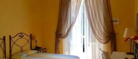 A room with two beds, a desk, a chair, and a window with curtains.