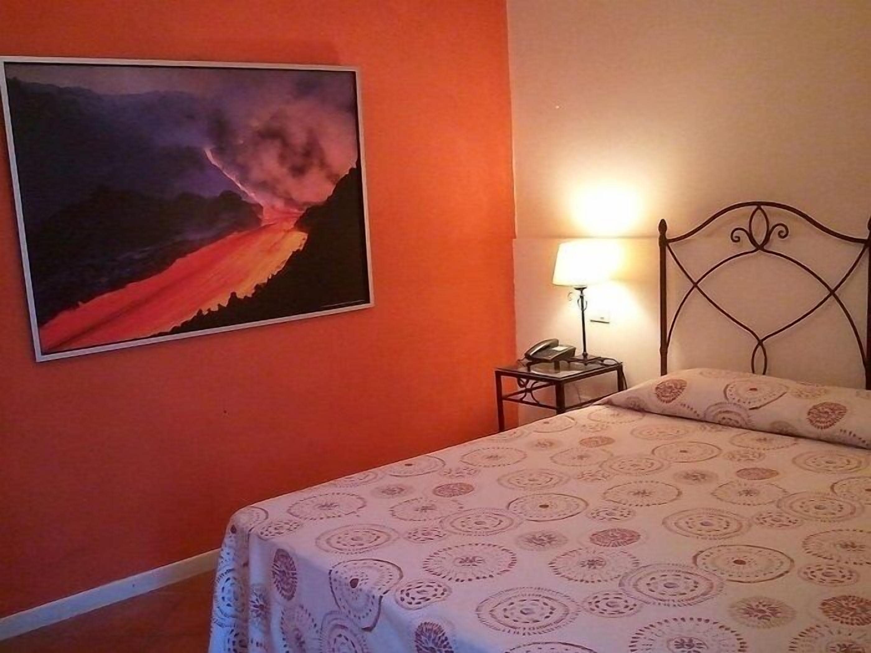 Een hotelkamer met een bed, nachtkastje, lamp en een schilderij aan de muur.