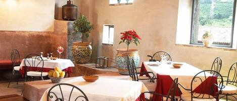 A restaurant with tables and chairs, a stone wall, and a window with a view.