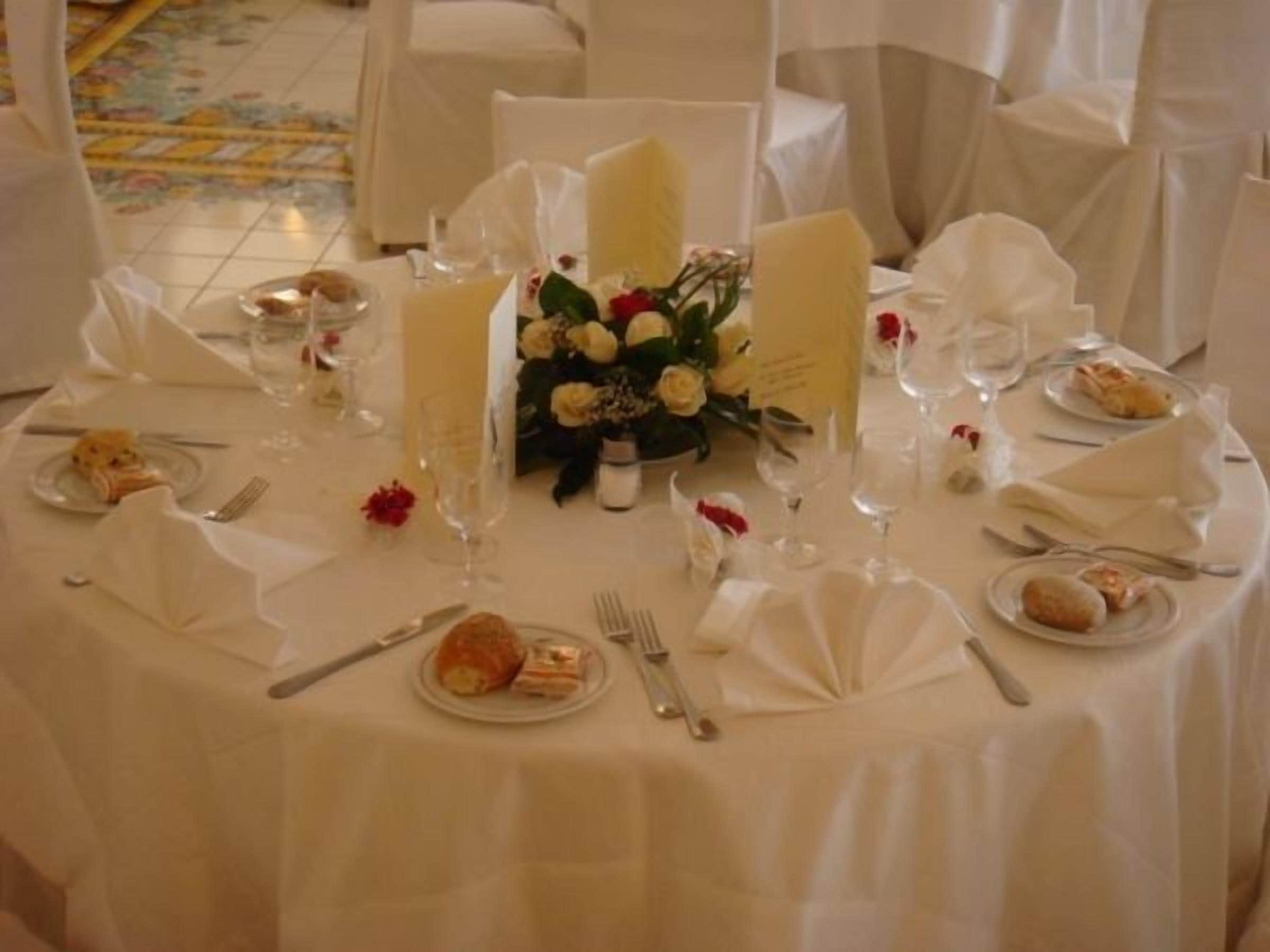 Ein runder Tisch, festlich gedeckt für eine Veranstaltung, mit weißen Tischdecken, Speisen, Weingläsern und einem Blumenarrangement in der Mitte.