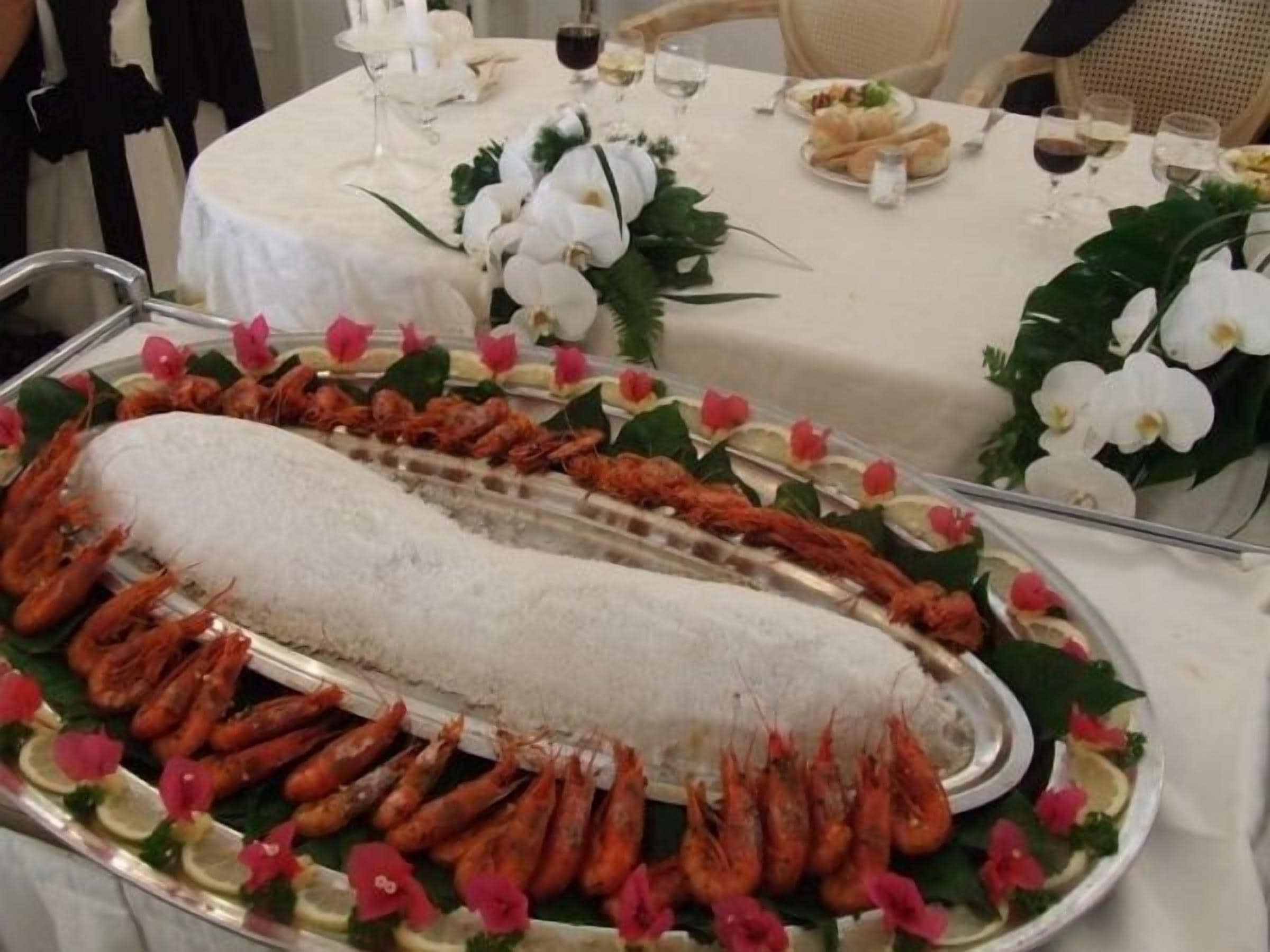 A seafood platter with shrimp and a large fish centerpiece, surrounded by decorative flowers and garnishes.