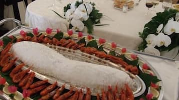A seafood platter with shrimp and a large fish centerpiece, surrounded by decorative flowers and garnishes.