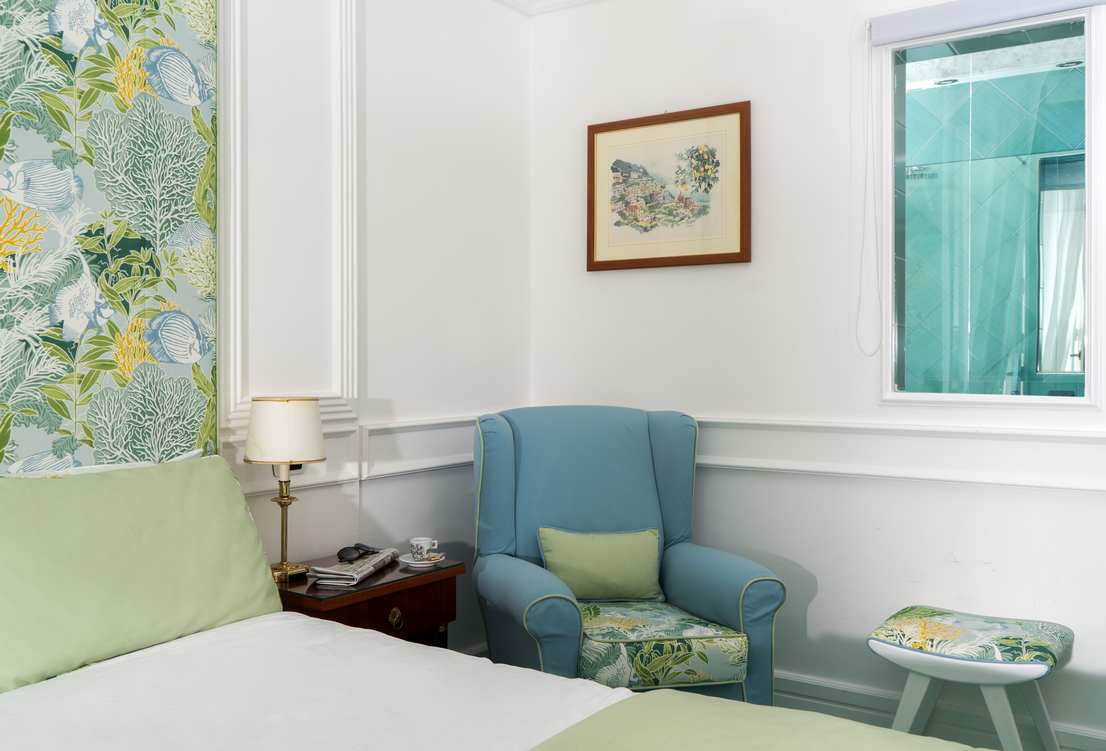 A bedroom with a bed, a chair, a small table, a lamp, and a framed picture on the wall.