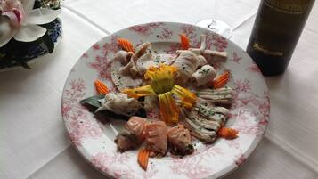 Um prato de comida com vários legumes e carne, um copo de vinho e um vaso decorativo com flores.