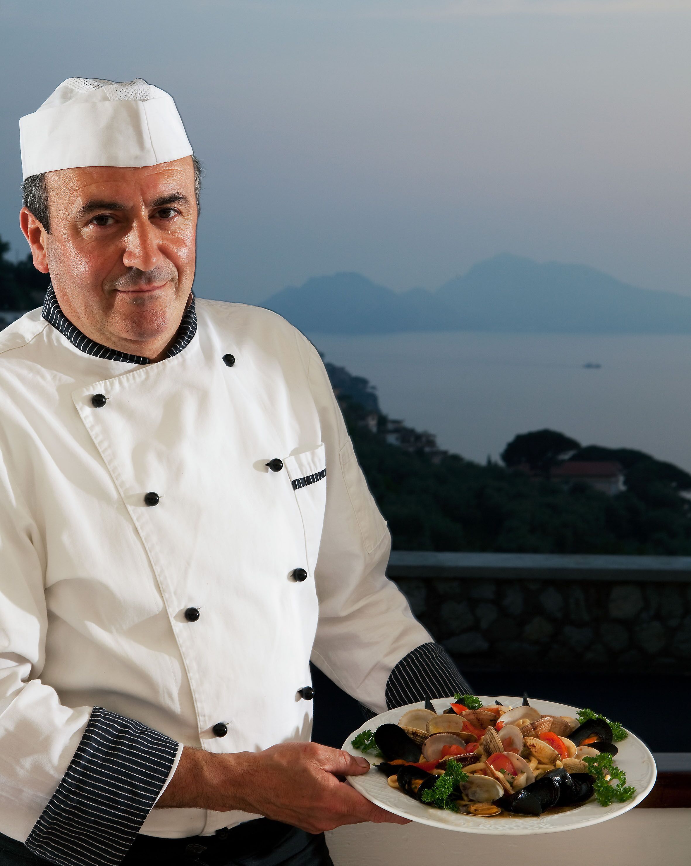 Un chef con uniforme blanco sostiene un plato de mariscos.