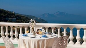 A table set on a balcony with a view of the sea and mountains.