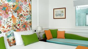 Habitación de hotel con cama, sofá verde, tapiz colorido, cuadro en la pared y ventana.