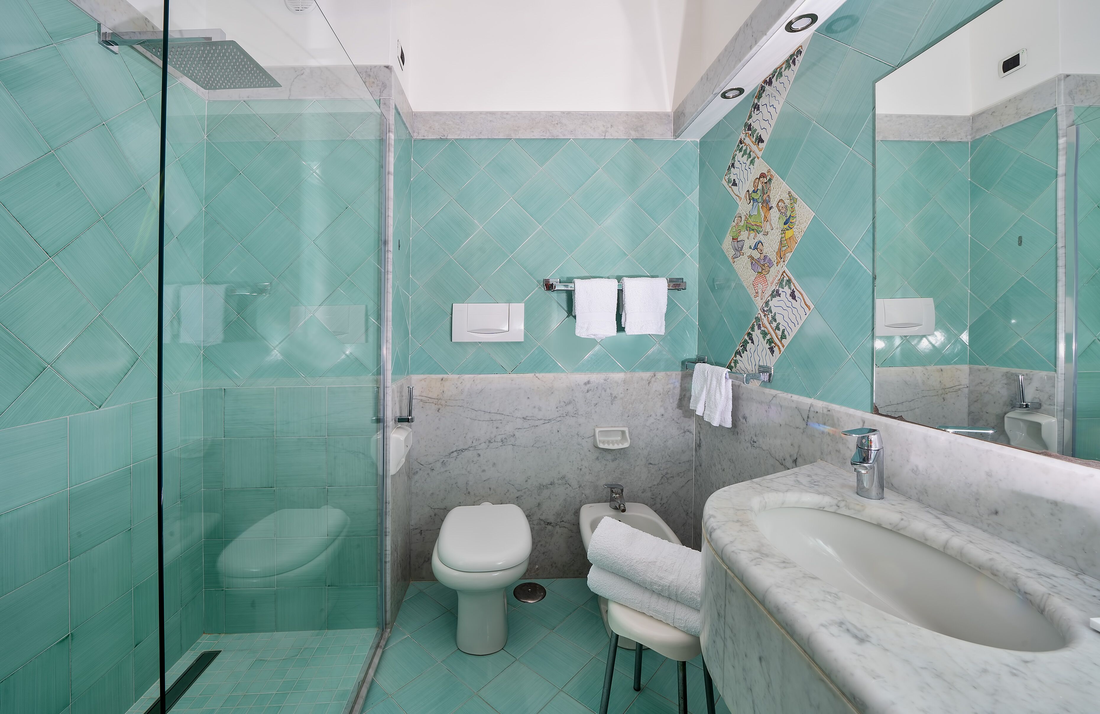 Un bagno con box doccia in vetro, un water, un bidet e un lavabo in marmo con specchio.