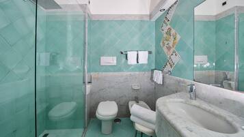 Un bagno con box doccia in vetro, un water, un bidet e un lavabo in marmo con specchio.