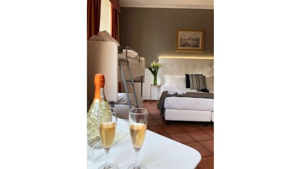 A room with a bed, a bedside table with two champagne flutes, and a nightstand with a lamp. - 207 Inn (Rome)