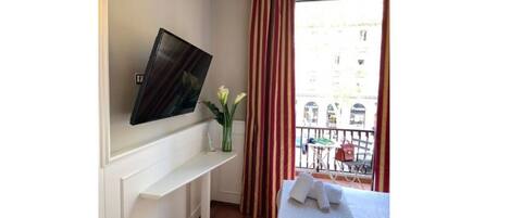 Una habitación con un televisor de pantalla plana en la pared, un tocador blanco y una ventana con vistas a la ciudad.