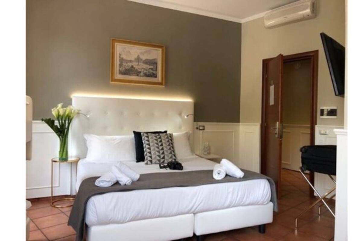Una habitación de hotel con una cama, una mesita de noche, un jarrón con flores y un cuadro en la pared.
