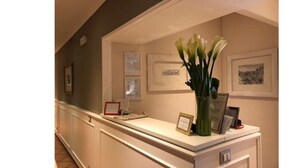 A reception area with a counter, framed certificates, and a vase with green leaves. - 207 Inn (Rome)