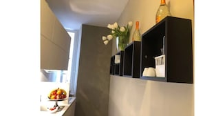 A narrow hallway with a white wall, a small table with a fruit bowl, and a shelf with various items including a bottle and a vase with flowers. - 207 Inn (Rome)