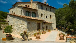 A stone building with a tiled roof, multiple windows, and a paved entrance area with potted plants.