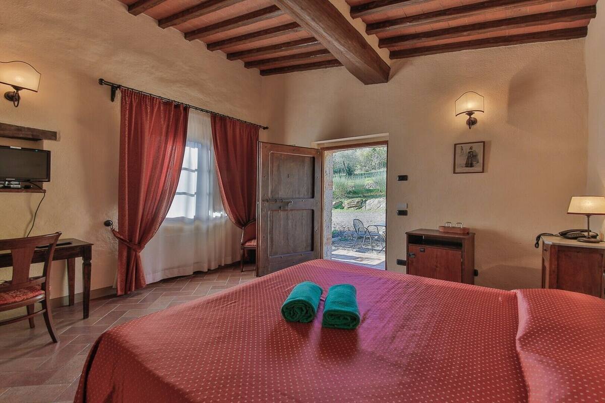 A bedroom with a bed, a desk, a television, and a door leading outside.