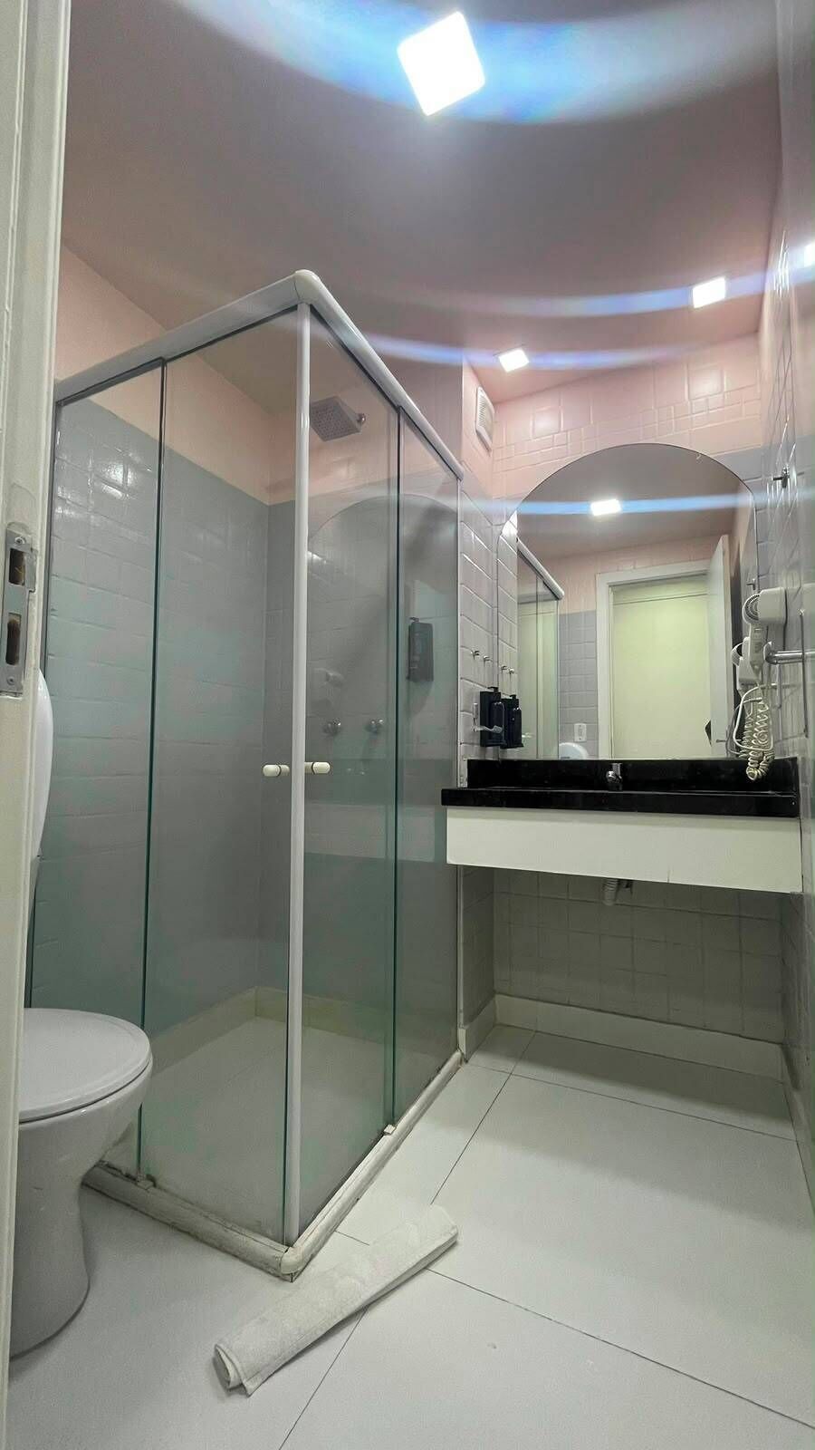 A bathroom with a glass-enclosed shower, a toilet, and a sink with a mirror above it.