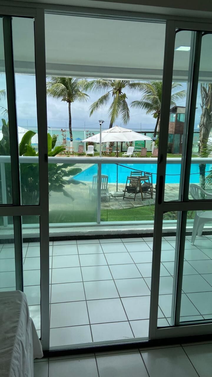 A room with a sliding glass door leading to a pool area with palm trees and outdoor furniture.