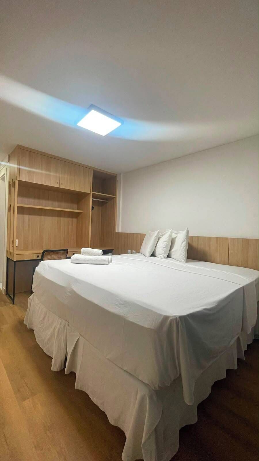 A hotel room with a large bed, a desk, and a wardrobe.